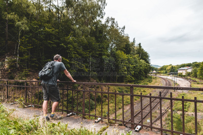 A tourist looks down from a viaduct onto a railroad track and a small railway station Jedlina-Zdrój, surrounded by forest, southwest Poland.