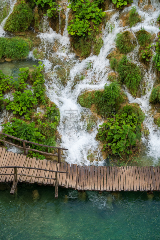 Wooden walkway passing one of the famous natural water cascades at the Plitvice Lakes National Park. 
Plitvička Jezera, Croatia - June 25th 2019 - Official photography permission obtained by the Plitvice Lakes National Park and available on request.